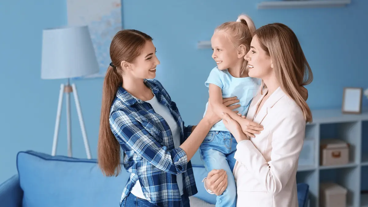 Two women smiling with a young child in a living room
