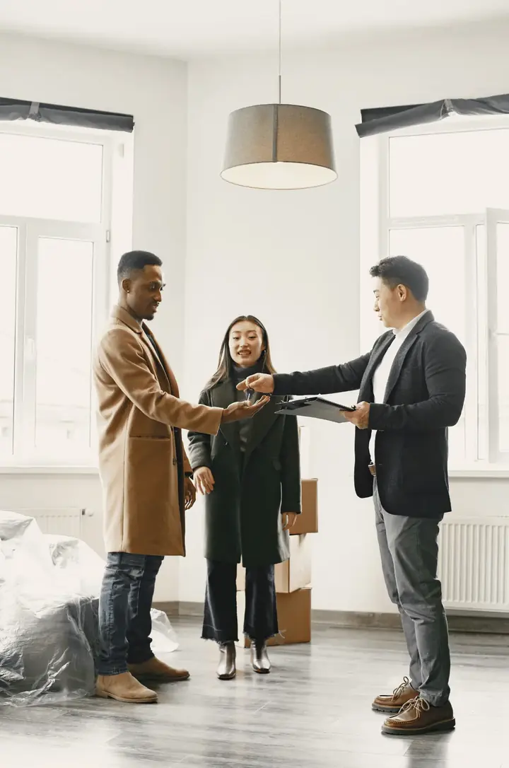An agent handing house keys to a couple in an empty, bright living room