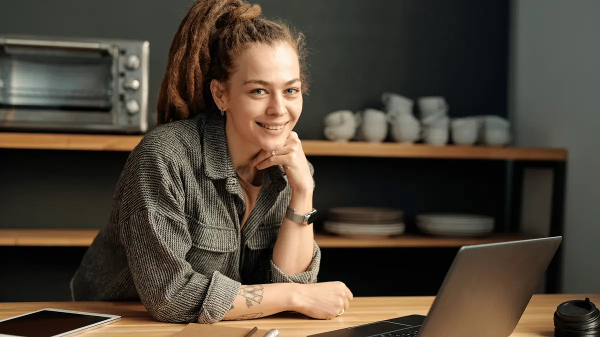 Smiling business owner leaning on a desk next to a laptop