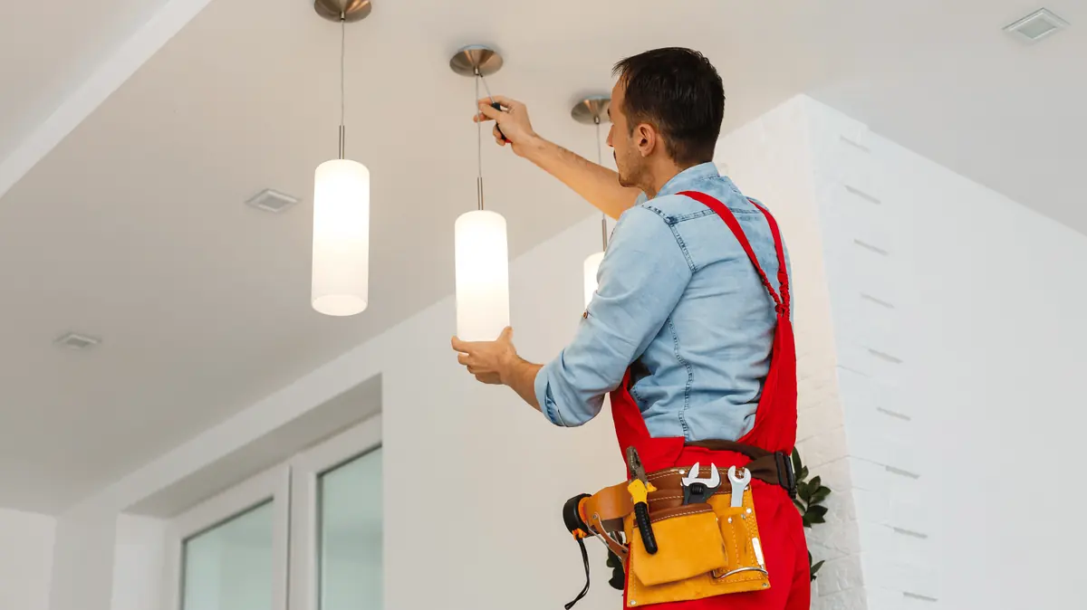 An electrician installing pendant lights on a ceiling